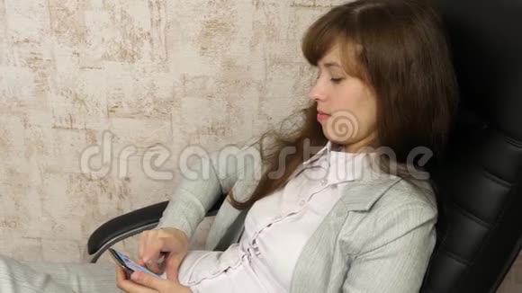 办公室里的女人在工作场所休息漂亮的女商人带着电话坐在椅子上光着脚在桌子上视频的预览图