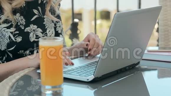 美丽的金发女郎在夏日露台的咖啡馆里用笔记本电脑打字视频的预览图