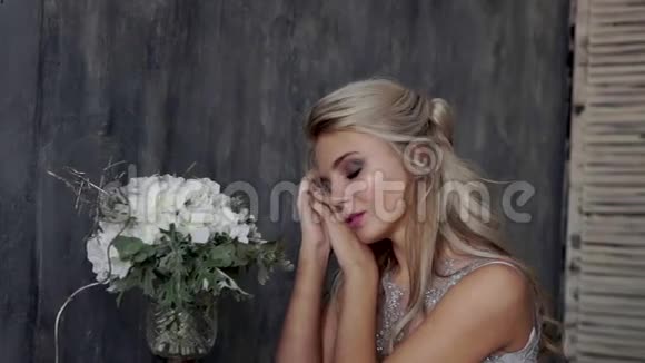 漂亮的金发女人模特穿着婚纱坐在椅子上灰色背景上有一束花视频的预览图