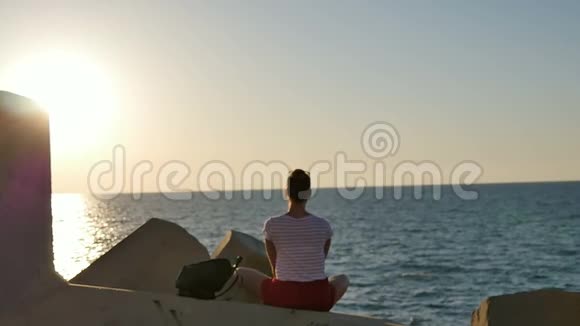 梦中的年轻女子坐在岩石上享受日落时的大海视频的预览图