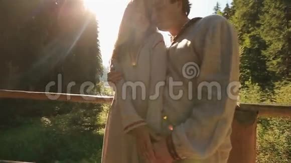美丽的年轻夫妇穿着传统的乌克兰服装在山上的木桥上轻轻地接吻雄伟壮观视频的预览图