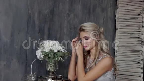 漂亮的金发女人模特穿着婚纱坐在椅子上灰色背景上有一束花视频的预览图
