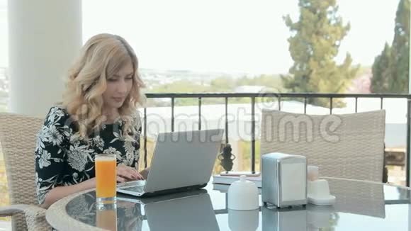 令人印象深刻的女人坐在一家咖啡馆里喝着一杯橙汁在笔记本电脑上输入一条信息视频的预览图
