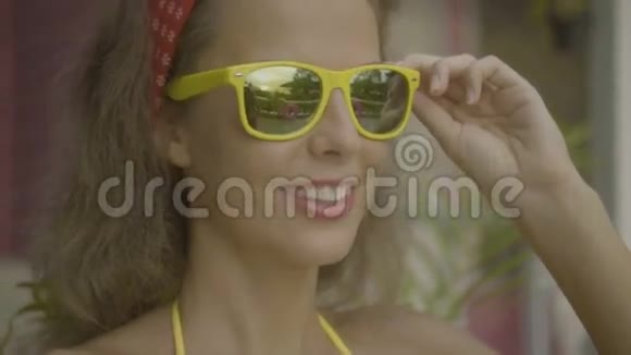 漂亮的年轻快乐的女人穿着比基尼脱下和戴上其他太阳镜孤立在粉红色的房子的背景上视频的预览图