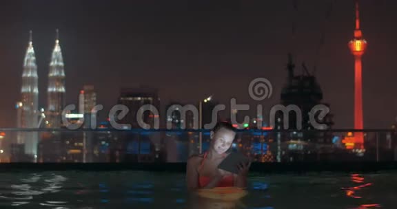 吉隆坡夜晚屋顶泳池有垫子的女人视频的预览图