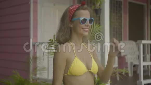 漂亮的年轻快乐的女人穿着比基尼脱下和戴上其他太阳镜孤立在粉红色的房子的背景上视频的预览图