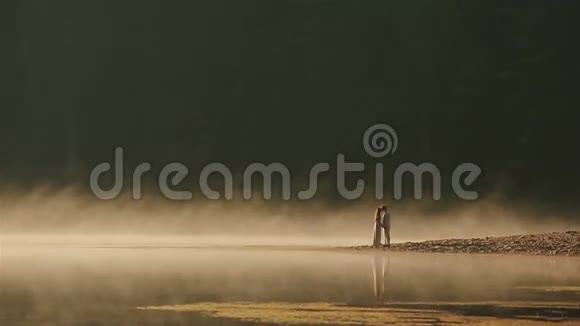 一对身着乌克兰民族服装的快乐乡村夫妇在落日的金色薄雾中亲吻岩石海岸视频的预览图