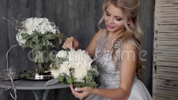 一位漂亮的金发女子模特穿着婚纱坐在椅子上灰色背景上放着一束鲜花视频的预览图