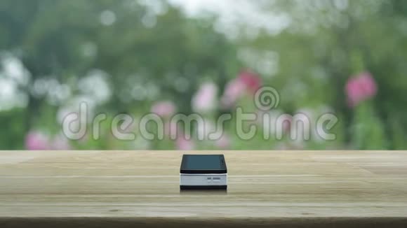 现代智能手机屏幕上的麦克风平板图标在木桌上在公园的粉红色花朵和树木上模糊商务交流视频的预览图