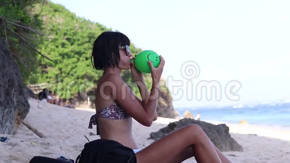 年轻的女人吹着一个绿色的气球年轻的女人在海滩上海洋巴厘岛印度尼西亚视频的预览图
