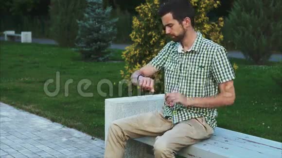 坐在公园里用智能手表的年轻人视频的预览图