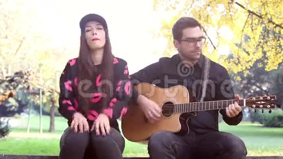 一对情侣坐在公园的长凳上弹吉他视频的预览图
