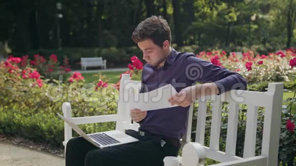 公园里的年轻人用笔记本电脑和纸视频的预览图