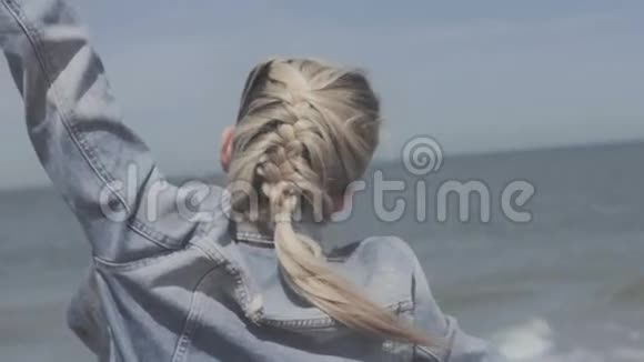 穿着牛仔夹克的快乐金发女人在孤独的海滩上亲吻视频的预览图