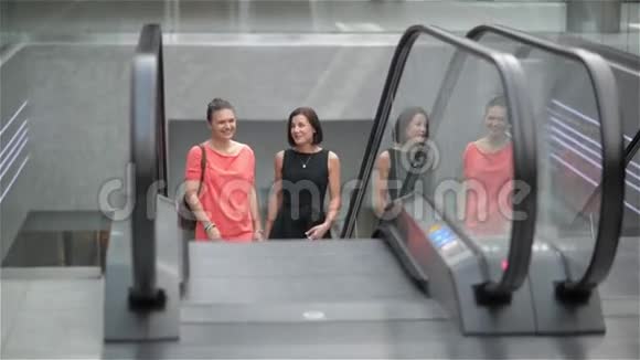 两个女孩在商场的自动扶梯上楼朋友们在商店里购物视频的预览图