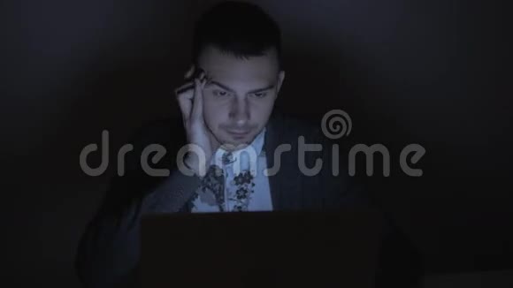 商人在晚上和电脑一起工作忙碌而疲惫的自由职业者红眼睛笔记本电脑上的蓝色屏幕视频的预览图