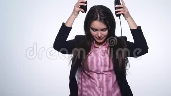 微笑着快乐的年轻女子用耳机听音乐在白色背景下孤立地跳舞视频的预览图