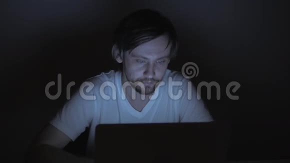 商人在晚上和电脑一起工作忙碌而疲惫的自由职业者红眼睛笔记本电脑上的蓝色屏幕视频的预览图