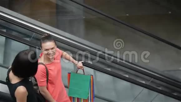 年轻漂亮的快乐女人在商场的自动扶梯上女孩在商店里购物视频的预览图