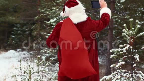 圣诞老人在白雪皑皑的树林里用平板电脑拍摄视频的预览图