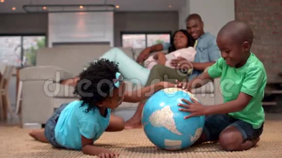 孩子们看着地板上的地球仪而父母看着视频的预览图