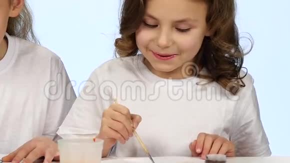 幼儿坐在桌子旁用颜色装饰图纸白色背景慢动作视频的预览图