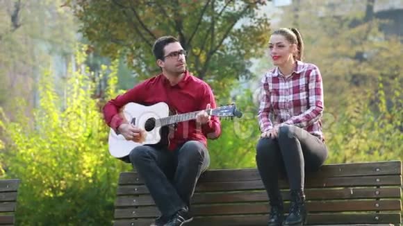 男人和女人坐在公园的长凳上弹吉他玩得开心视频的预览图