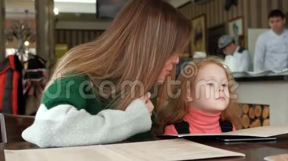 美丽的女人和她的女儿在一家披萨店咖啡馆看菜单视频的预览图