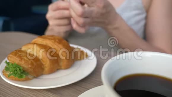 一个面目全非的女人有着漂亮的领口在咖啡馆里吃早餐还有一个羊角面包三明治里面有煮猪肉和视频的预览图