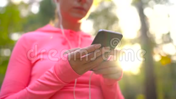 带着耳机和智能手机的女人选择音乐穿过秋天公园视频的预览图