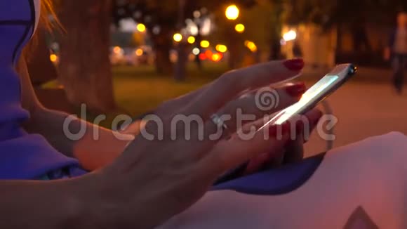 穿着红色指甲油的女孩在晚上的街道上使用她的智能手机4K视频视频的预览图