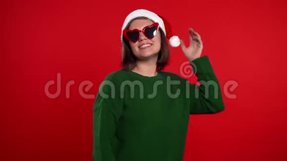 年轻女子微笑着在红色的背景上跳舞戴圣诞圣诞圣诞帽的女孩视频的预览图
