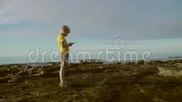 可爱的男孩在海滩上拿着智能手机视频的预览图