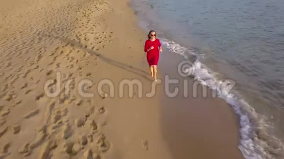 一个女人赤脚在潮湿的沙滩上奔跑的俯视图海浪冲刷着沙滩上的脚印视频的预览图