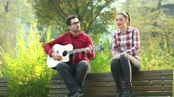 男人和女人坐在公园的长凳上弹吉他玩得开心视频的预览图