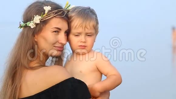 母亲穿着黑色连衣裙和花环手里拿着儿子在海滩上视频的预览图