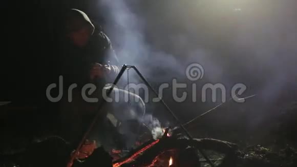 白种人坐在篝火旁晚上使用智能手机视频的预览图