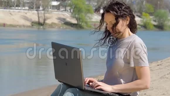 带着笔记本电脑的女孩在河边的新鲜空气中工作春天的晴天视频的预览图