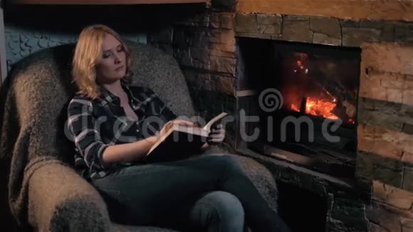 美丽的年轻女子读书书坐在壁炉旁假日及生活方式概念视频的预览图