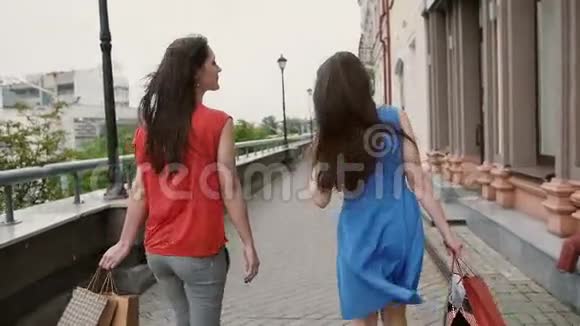 两个年轻漂亮的女朋友拿着购物袋走着谈着玩后景慢镜头视频的预览图