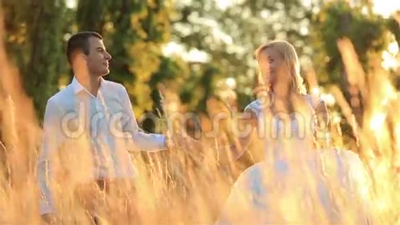 年轻漂亮的新婚夫妇走在金色的麦田里背景下美丽的日落视频的预览图