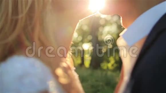 美丽的金发新娘和英俊的新郎在壮丽的夕阳下温柔地接吻视频的预览图