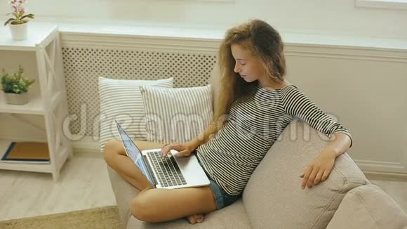 快乐少女在沙发上使用笔记本电脑视频的预览图