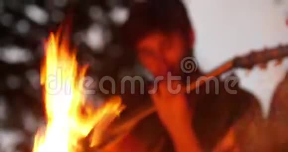 森林里坐在篝火旁弹吉他的年轻男女视频的预览图
