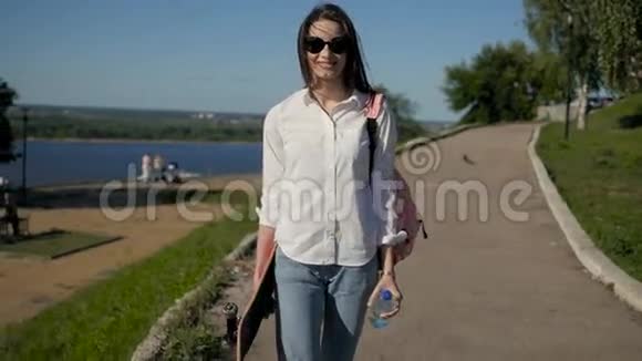 年轻漂亮的女孩拿着滑板在公园散步视频的预览图