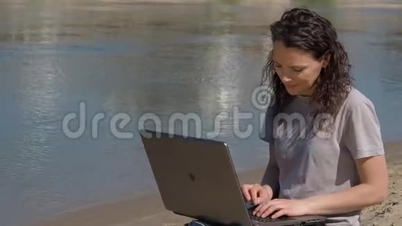 带着笔记本电脑的女孩在河边的新鲜空气中工作春天的晴天视频的预览图
