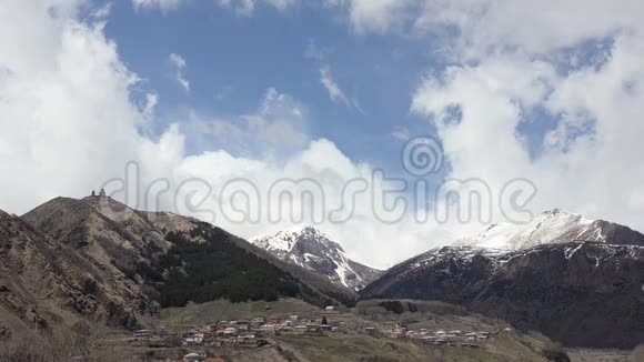 在白云的背景下在山上看到山村和圣三位一体Gergeti神庙视频的预览图