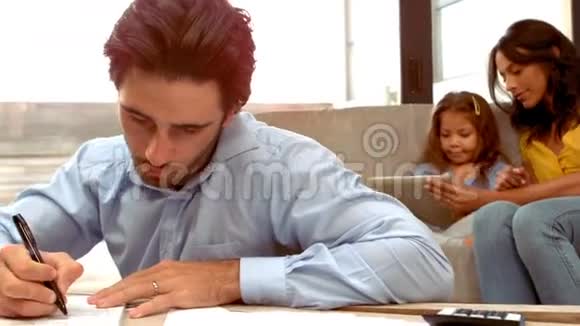 西班牙裔男子一边工作一边妻子和女儿躺在沙发上视频的预览图