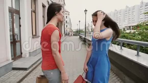两个年轻漂亮的女朋友拿着购物袋走着谈着玩后景慢镜头视频的预览图