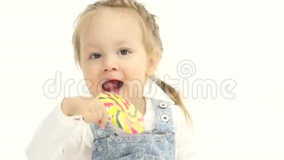 小女孩手里拿着一颗甜糖果舔它白色背景视频的预览图
